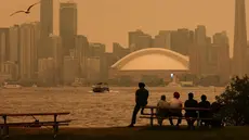 Warga memandang cakrawala pusat kota Toronto dari Kepulauan Toronto saat kabut asap akibat kebakaran hutan di Ontario Utara menyelimuti kota dan menurunkan kualitas udara, Toronto, Ontario, Kanada, Kamis, 15 Juli 2026. (AFP/ Cole Burston)