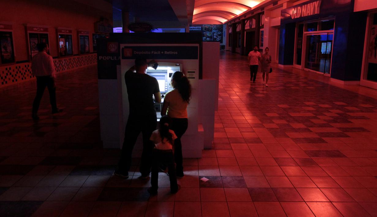 Warga menggunakan mesin ATM di pusat perbelanjaan ketika pemadaman listrik di San Juan, Puerto Rico, Rabu (21/9). Kebakaran yang terjadi di pembangkit listrik Puerto Rico menyebabkan 1,5 juta penduduk pulau itu hidup tanpa listrik. (REUTERS/Alvin Baez)