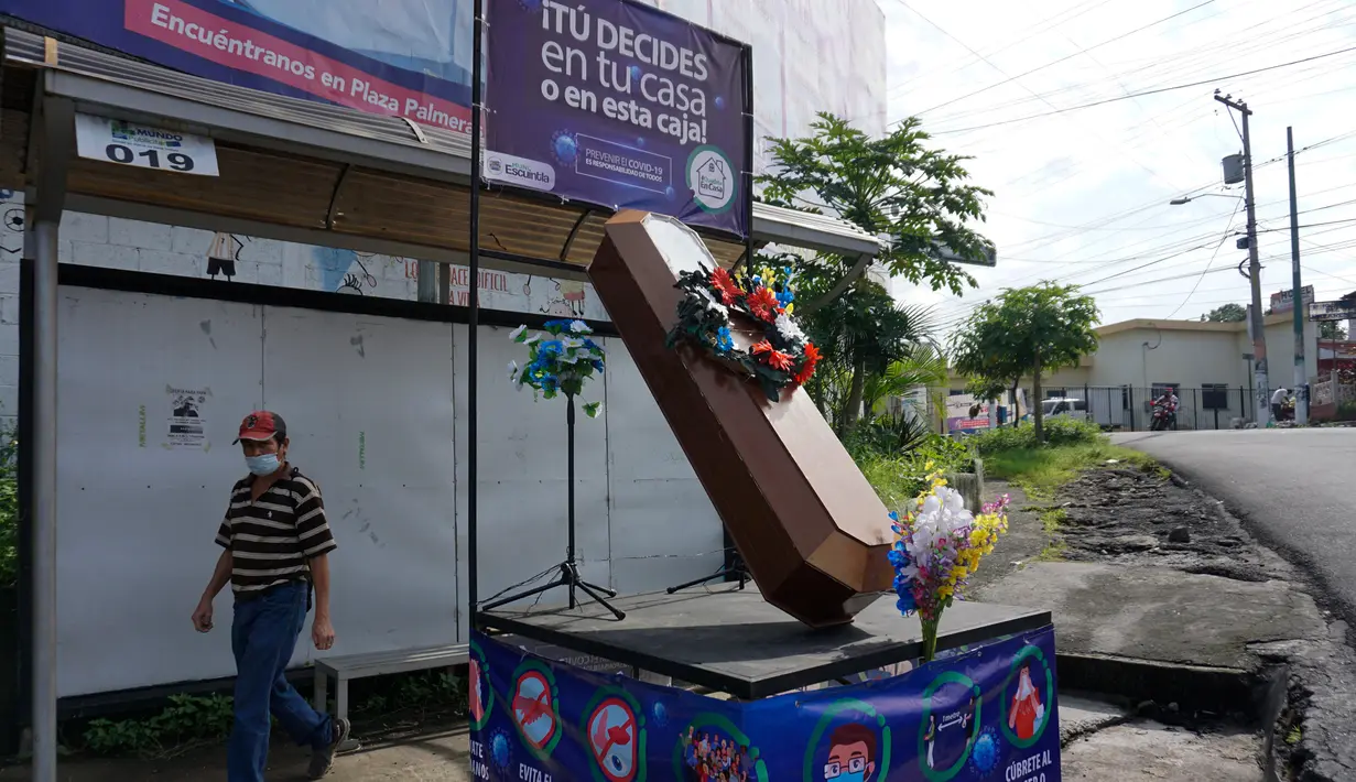 Warga berjalan dekat peti mati dengan tulisan, "Anda memutuskan, di rumah atau di dalam kotak ini", sebagai bagian dari kampanye pemerintah setempat di jalan-jalan kotamadya Escuintla, Guatemala City pada 21 Juli 2020. Kampanye itu sebagai upaya menghentikan penyebaran COVID-19. (Johan ORDONEZ/AFP)