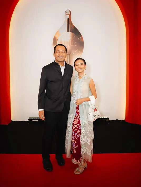 Kamila Andini tampil anggun dalam balutan kebaya tanpa lengan semi transparan dan kain batik merah. Sementara suaminya mengenakan setelan hitam. [@kamilandini]