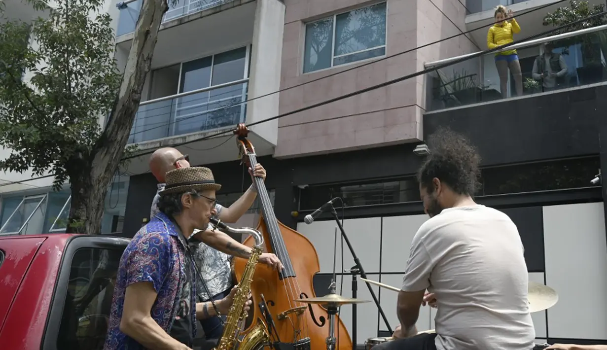 Warga (kanan) menyaksikan band Maroto Jazz Trio yang terdiri dari Diego Maroto pada Saxophone, Jorge Molina pada double bass, dan Edy Vega pada drum tampil dari atas sebuah van melewati kawasan Mexico City, Meksiko, 29 Agustus 2020. (RODRIGO ARANGUA/AFP)
