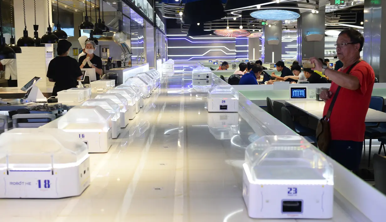 Pengunjung mengambil gambar sejumlah robot pintar sebesar oven microwave di restoran Robot.He milik Alibaba di Shanghai, 30 Juli 2018. Tugas robot itu mengangkat tutup kaca hidangan bergaya Shanghai dan mengucapkan, "Selamat menikmati hidanganmu". (AFP)