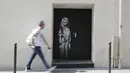 Seorang pria berjalan melewati mural yang diduga karya seniman sekaligus aktivis Banksy di Paris, Prancis, Minggu (24/6). Seniman jalanan misterius asal Inggris itu membuat mural bertema migrasi. (THOMAS SAMSON/AFP)