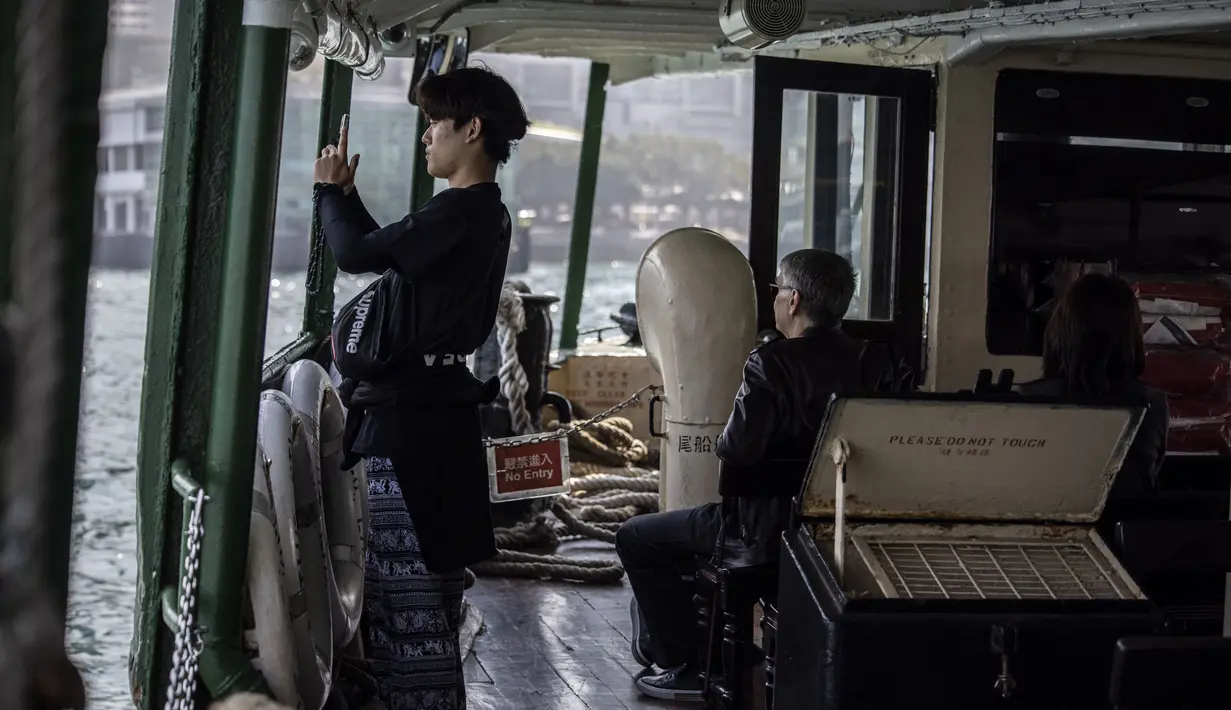 Seorang pria (kiri) berfoto saat menaiki Star Ferry di Hong Kong (1/3/2023). Pemerintah Hong Kong mengumumkan pelonggaran aturan Covid-19 dengan mencabut mandat penggunaan masker pada 1 Maret. Kini, warga Hong Kong bebas seperti sebelum pandemi. (AFP/Isaac Lawrence)