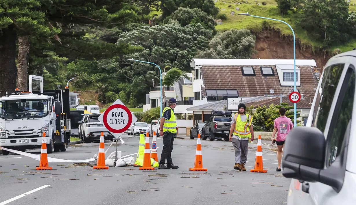 Ratusan keluarga yang berada di lokasi perkemahan telah dievakuasi. Tampak dalam foto, petugas darurat menutup jalan setelah tanah longsor sementara pencarian sedang dilakukan oleh layanan darurat setempat untuk orang hilang di Gunung Maunganui, Tauranga, Selandia Baru pada Kamis 22 Januari 2026. (DJ MILLS/AFP)