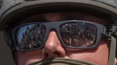 Para pengunjuk rasa yang memegang tanda dan bendera tercermin dalam kacamata yang dikenakan Garda Nasional California yang berdiri di luar Gedung Federal saat mereka memprotes operasi imigrasi federal di Los Angeles, Amerika Serikat pada 9 Juni 2025. (Apu GOMES/AFP)