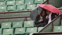 Dua orang penonton menunggu hujan reda  pada laga antara Richard Gasquet dan Kei Nishikori pada turnamen Prancis Terbuka 2016 di Roland Garros, (28/5/2016). (AFP/Thomas Samson)