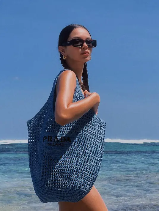 Alyssa Daguise berjemur menggunakan bikini. Namun tertutup oleh tas Raffia Tote dari seri Tropico milik Prada berwarna biru yang dijinjingnya. (instagram/alyssadaguise)