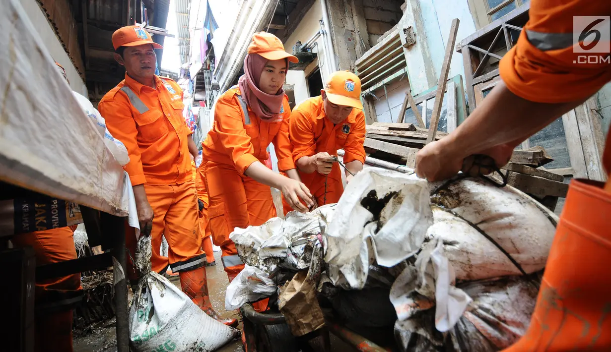 Petugas PPSU Kelurahan Kampung Melayu Siti Hajar bersama rekan-rekannya membawa karung lumpur membersihkan sisa lumpur akibat banjir yang melanda Kebon Pala, Jakarta, Kamis (25/4). (Liputan6.com/Herman Zakharia)