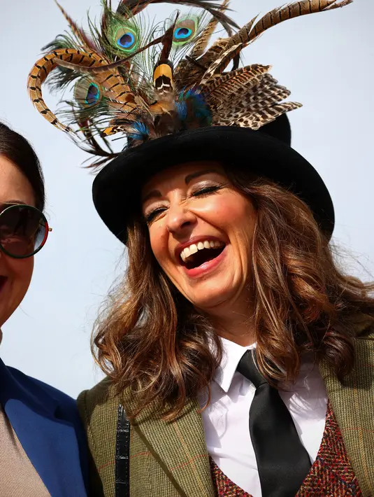 Seorang wanita tertawa saat tiba pada hari pertama Festival Cheltenham di Cheltenham Racecourse, di Cheltenham, Inggris (15/3/2022). Kehadiran para wanita memberikan nuansa tersendiri di kompetisi pacuan kuda tersebut. (AFP/Adrian Dennis)
