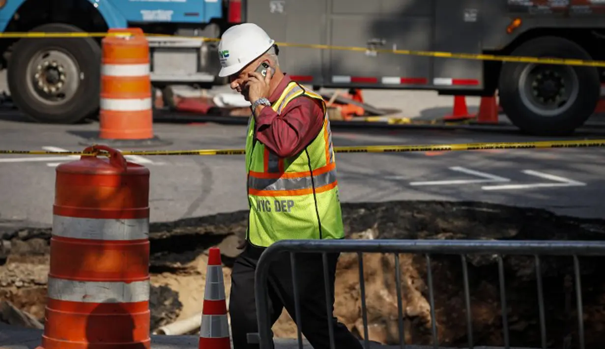 Seorang petugas berjalan di dekat lubang besar (sinkhole) di wilayah Brooklyn, New York, Selasa (4/8/2015). Lubang yang terbentuk di persimpangan pemukiman Sunset Park itu disebabkan erosi dan merusak pipa air serta aspal jalan. (AFP/Kena Betancur)