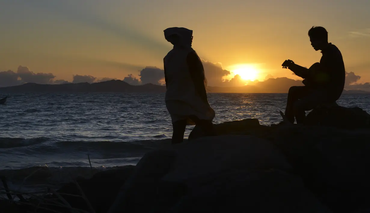 Seorang pria memainkan gitar saat matahari terbenam atau sunset di pantai Banda Aceh pada 28 Juni 2019. Pemandangan makin sempurna saat matahari tenggelam hingga alam berubah semakin remang dan romantis. (Photo by CHAIDEER MAHYUDDIN / AFP)