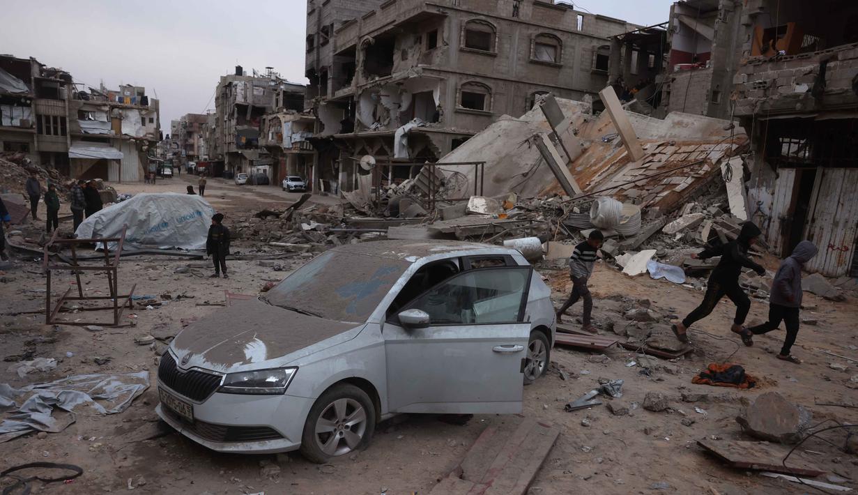 Otoritas kesehatan setempat mengonfirmasi bahwa dari total korban jiwa, enam di antaranya adalah anak-anak. Tampak dalam foto, para pemuda Palestina yang mengungsi berlari melewati mobil yang rusak dan puing-puing setelah pesawat Israel menargetkan sebuah rumah berlantai lima tadi malam, di Khan Yunis, Jalur Gaza selatan pada Kamis 6 Februari 2026. (Bashar Taleb/AFP)