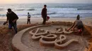 Seniman Palestina, Yazeed Abu Jarad, yang mengungsi dari Beit Lahia, membuat patung pasir dengan pesan ucapan "Selamat Datang, Ramadan" di sepanjang pantai di Khan Younis, selatan Gaza pada 17 Februari 2026. Tampak dalam foto, warga membantu seniman Palestina, Yazeed Abu Jarad, saat ia membuat patung pasir dengan pesan ucapan "Selamat Datang, Ramadan" di sepanjang pantai di Khan Younis, selatan Gaza pada 17 Februari 2026. (Bashar Taleb/AFP)