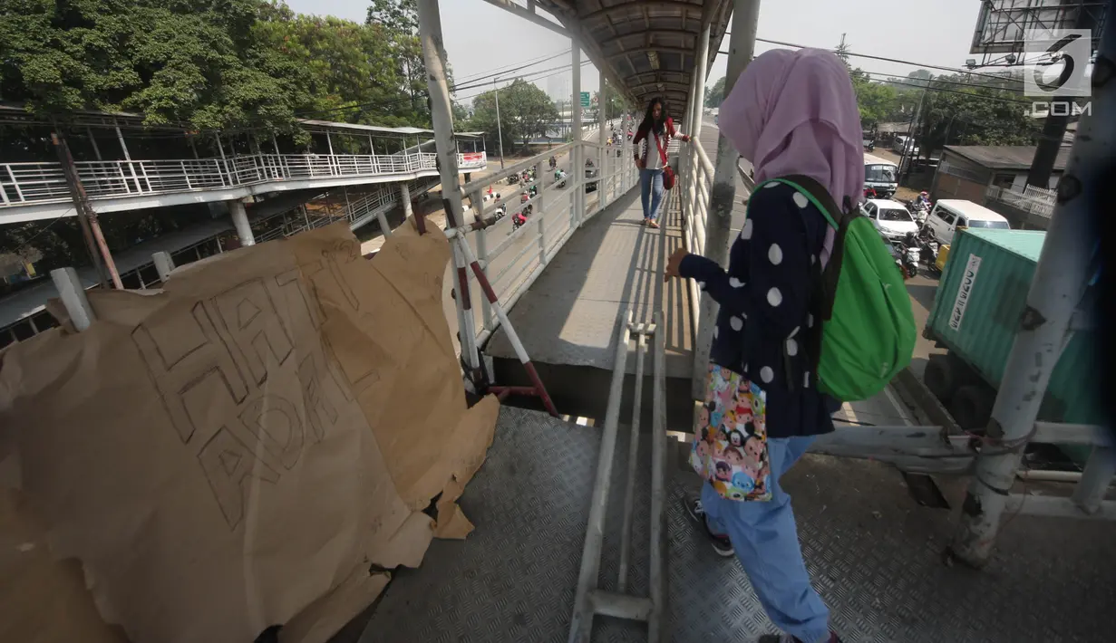 Pejalan kaki melewati lubang di atas JPO di Halte Bus Transjakarta di Jembatan Gantung, Cengkareng, Jakarta, Jumat (27/7). JPO yang rusak akibat tertabrak truk sejak setahun lalu hingga kini belum diperbaiki.  (Liputan6.com/Arya Manggala)