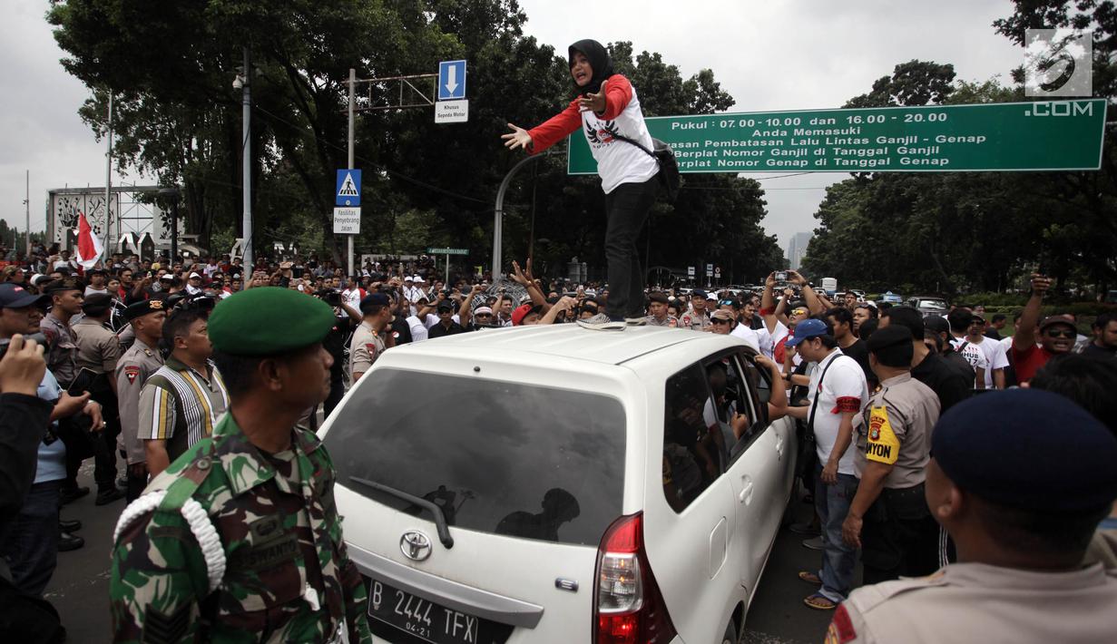 Seorang wanita naik di atas mobil taksi online yang melintas saat unjuk rasa di depan Istana Negara, Jakarta, Rabu (14/2). Kericuhan nyaris terjadi lantaran demonstran mencegat para driver online yang masih beroperasi. (Liputan6.com/Arya Manggala)