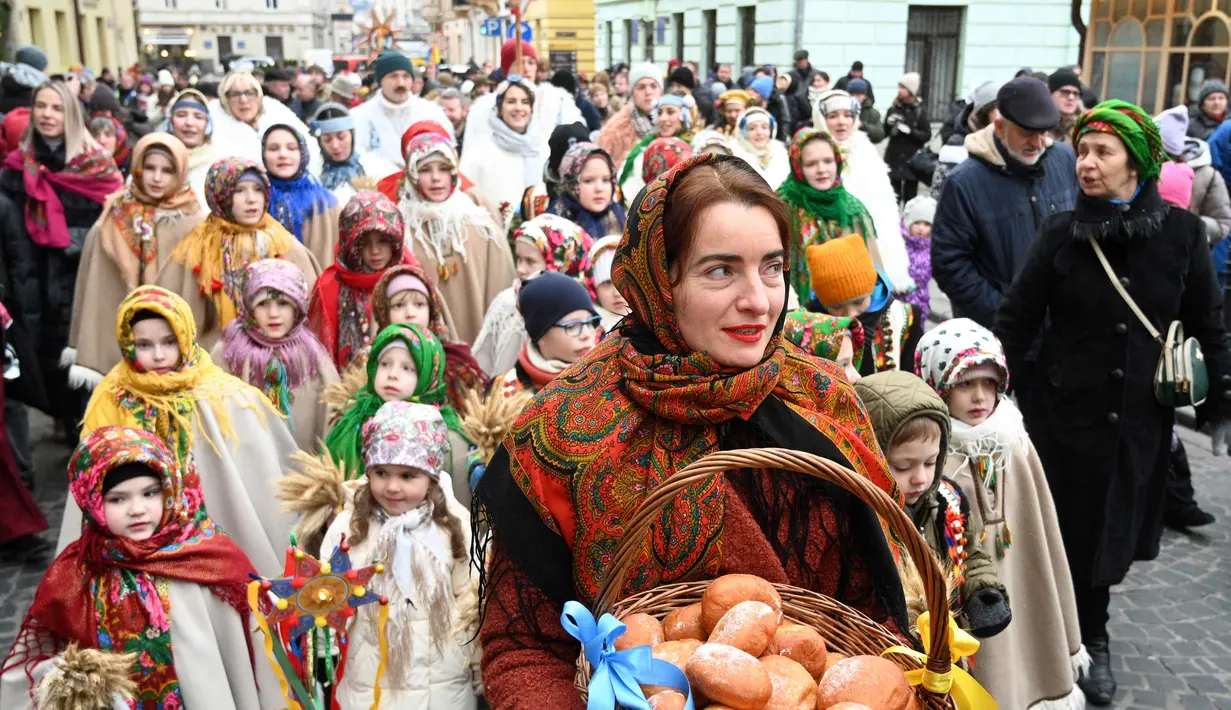 'Didukh' ditempatkan di sudut ruangan (biasanya di bawah ikon suci) selama Malam Natal. Tampak dalam foto, warga Ukraina yang mengenakan pakaian tradisional dan membawa hiasan Natal tradisional Ukraina 'Didukh' menyanyikan lagu-lagu rohani saat mereka mengikuti prosesi Malam Natal di Lviv pada 24 Desember 2025. (YURIY DYACHYSHYN/AFP)