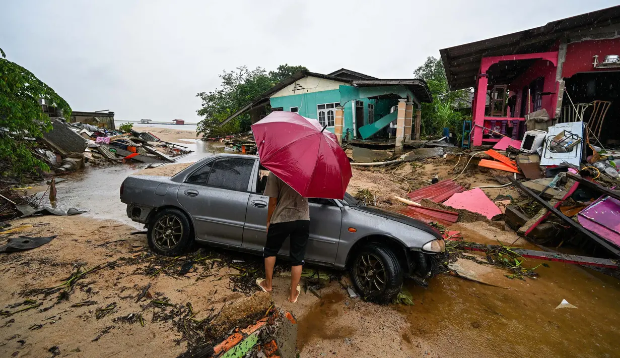 Seorang pria berjalan melewati sebuah mobil yang terdampar dan rumah-rumah yang rusak akibat banjir di Tumpat, negara bagian Kelantan, Malaysia, pada Rabu 4 Desember 2024. (MOHD RASFAN/AFP)