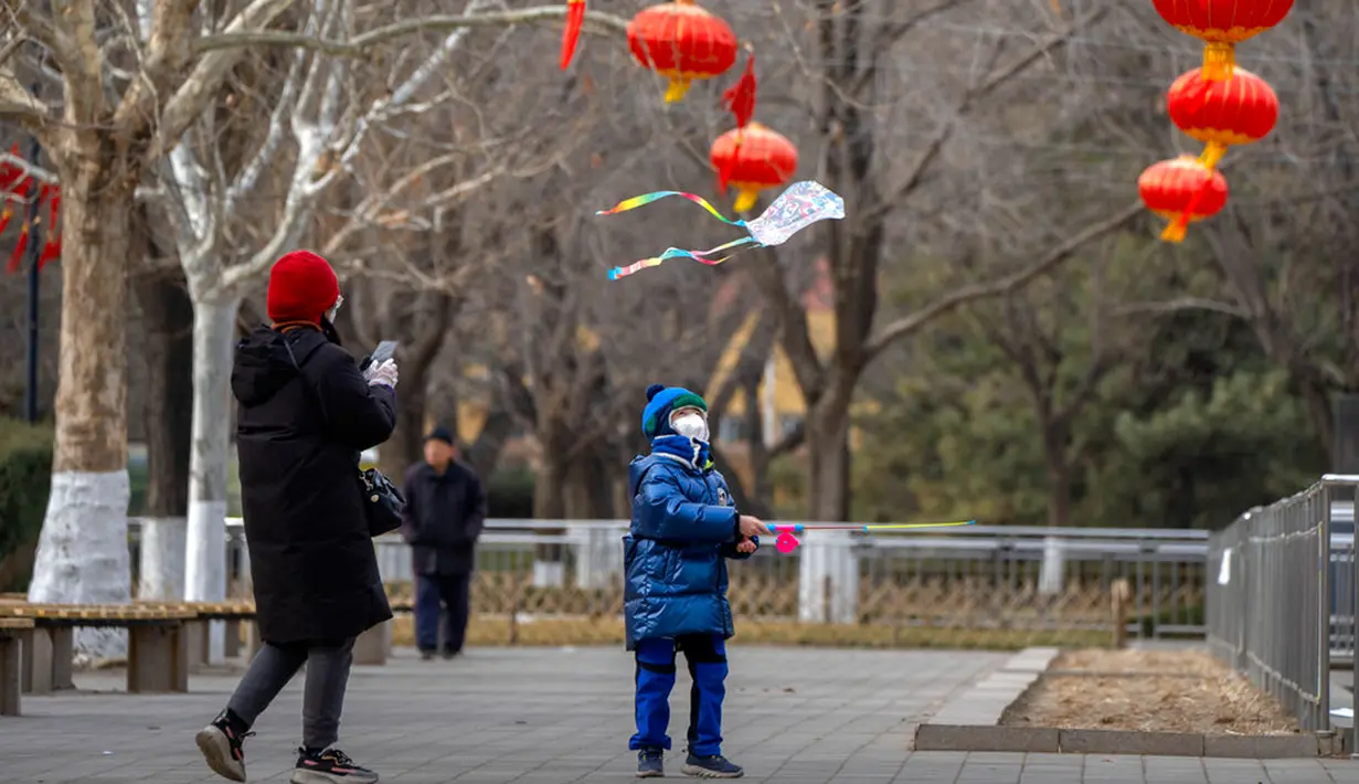 Seorang anak laki-laki yang mengenakan masker menerbangkan layang-layang dekat pohon berhias lentera di taman umum saat liburan Tahun Baru Imlek di Beijing, China, Kamis (26/1/2023). (AP Photo/Mark Schiefelbein)
