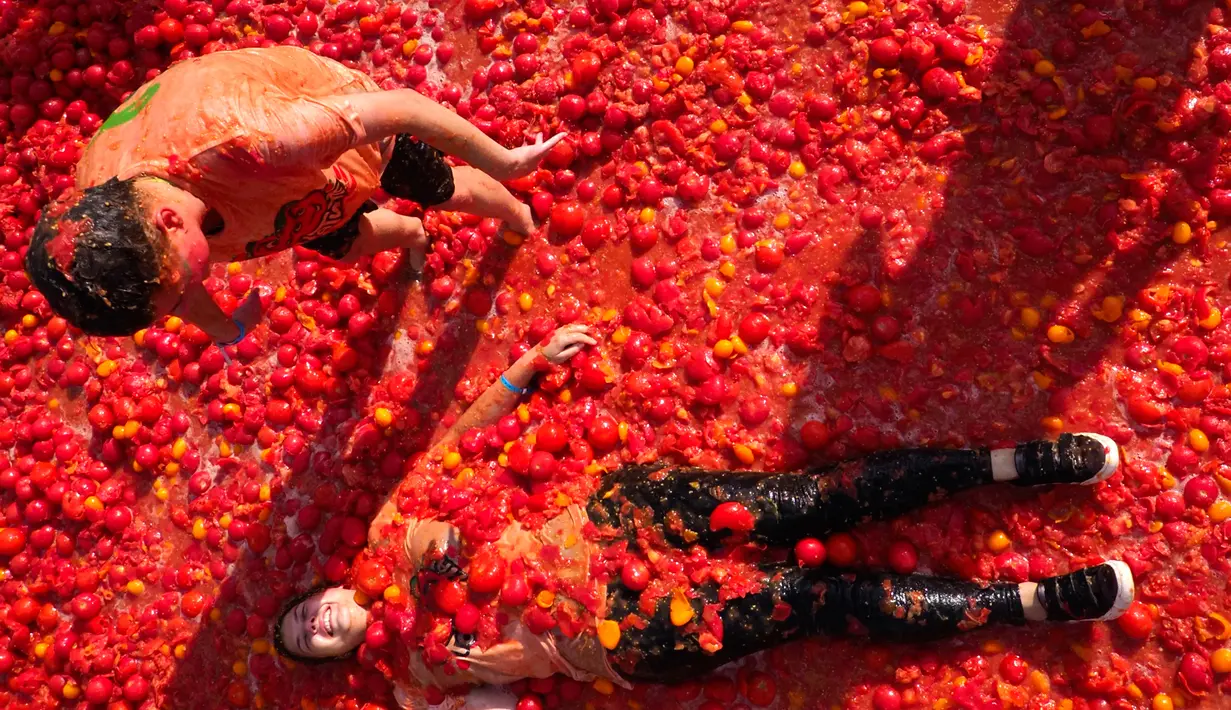 Peserta berbaring di atas tomat yang hancur ketika berpartisipasi dalam festival 'Tomatina' di St.Petersburg, Rusia, Minggu (18/8/2019). Tomatina atau perang tomat adalah festival Spanyol, dan tahun ini merupakan pertama kalinya dirayakan di Rusia. (AP Photo/Dmitri Lovetsky)