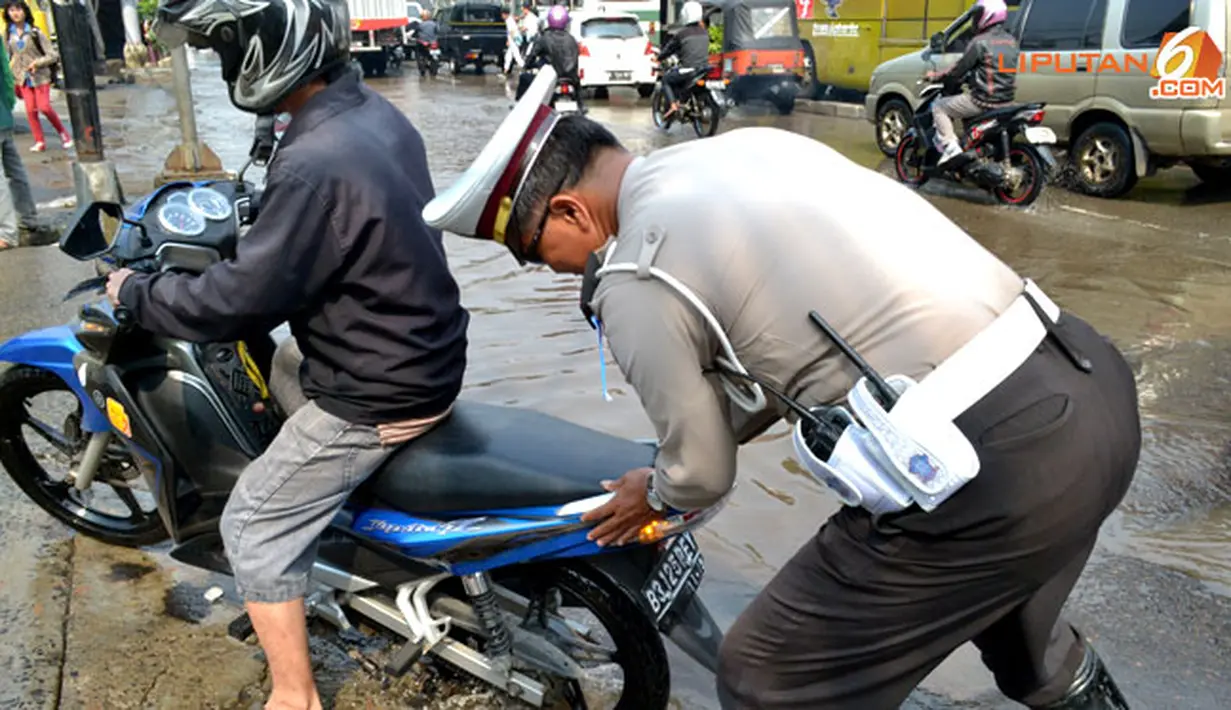 Polisi tengah membantu pengendara sepeda motor mogok karena genangan air yang masuk ke dalam mesin (Liputan6.com/Panji Diksana)
