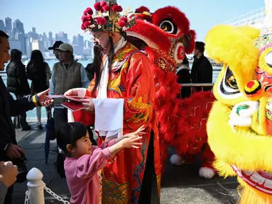 Seorang pria berpakaian seperti Cai Shen Ye atau Dewa Kekayaan Tionghoa membagikan dekorasi tradisional Fai Chun untuk keberuntungan dan kemakmuran di sebuah acara Tahun Baru Imlek di Hong Kong pada tanggal 10 Januari 2025. (Peter PARKS/AFP)