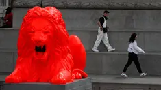 Wisatawan berjalan di dekat singa fluorescent merah yang bergabung dengan empat singa tradisional lainnya di Trafalgar Square di London (19/9). Patung Singa merah tersebut dipajang sebagai bagian dari Festival Desain London. (AP Photo/Frank Augstein)