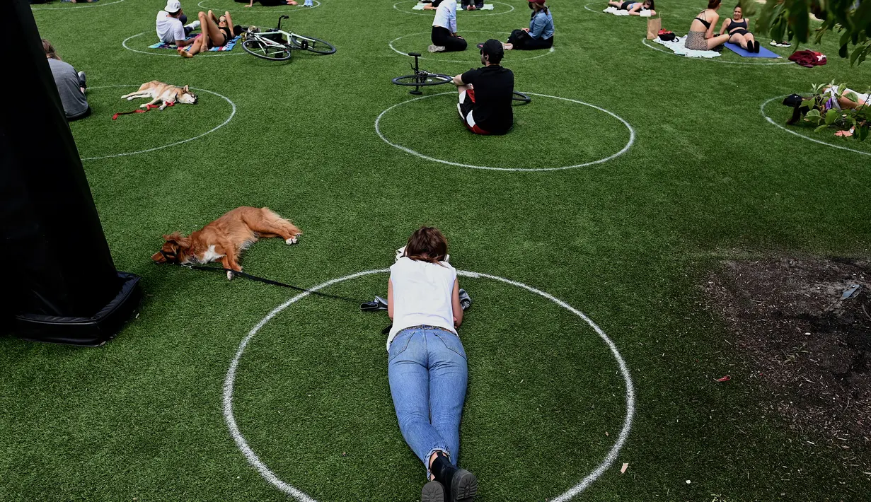 Orang-orang berusaha menjaga jarak dalam lingkaran putih saat bersantai di Domino Park, Brooklyn di Kota New York, Minggu (17/5/2020). Pengunjung taman berjemur dengan tetap menerapkan protokol penularan coorna Covid-19. (Photo by Johannes EISELE / AFP)