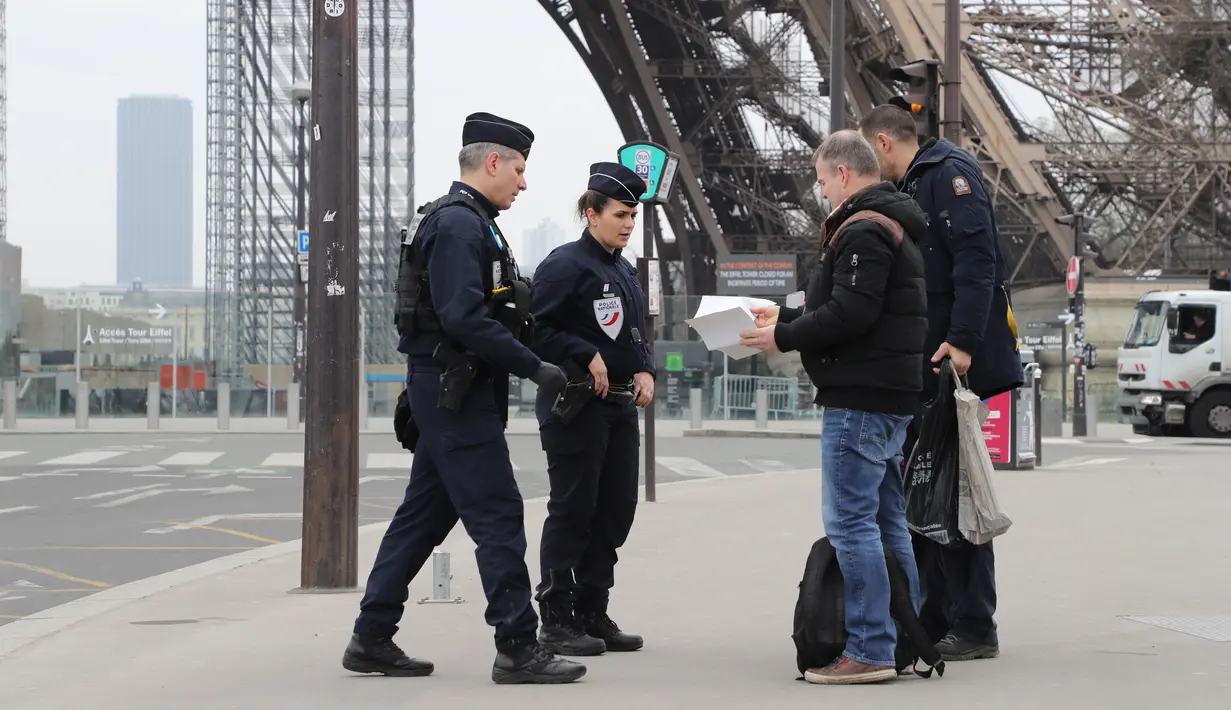 Polisi memeriksa dokumen warga saat lockdown di depan Menara Eiffel, Paris, Prancis, Rabu (18/3/2020). Prancis mengerahkan puluhan ribu polisi untuk berpatroli selama lockdown akibat virus corona COVID-19. (Ludovic MARIN/AFP)