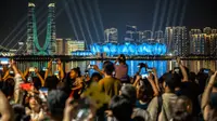 Orang-orang berkumpul di kawasan pejalan kaki Sungai Qiantang untuk menyaksikan pertunjukan cahaya di Hangzhou Olympic Sports Centre Stadium (kanan) menjelang Asian Games 2023 di Hangzhou, Provinsi Zhejiang, China, Selasa (19/9/2023). Hangzhou Olympic Sports Centre Stadium merupakan lokasi pembukaan Asian Games 2023. (Philip FONG/AFP)