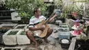 Bone bermain gitar di sela merawat ternak ikan cupang hias di workshop Bone's Costum Guitar, Jakarta, Rabu (10/3/2021). Untuk mencukupi kebutuhan sehari-hari, ayah dari 4 anak ini mencari sampingan dengan membuka ternak cupang hias sembari menunggu pelanggan gitar. (merdeka.com/Iqbal S Nugroho)