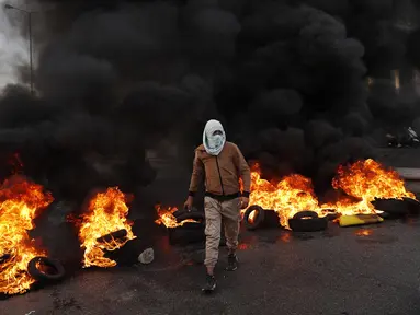 Seorang pengunjuk rasa melewati ban yang terbakar di sepanjang jalan raya utama yang mengarah ke Bandara Internasional Beirut selama protes terhadap kenaikan harga barang-barang konsumen dan jatuhnya mata uang lokal di Beirut, Lebanon, Senin (29/11/2021). (AP Photo/Hussein Malla)