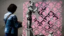 Seorang wanita melihat foto usai mengambil gambar mural yang diduga karya seniman sekaligus aktivis Banksy di Paris, Prancis, Minggu (24/6). Banksy terkenal dengan seni mural luar ruangan. (PHILIPPE LOPEZ/AFP)