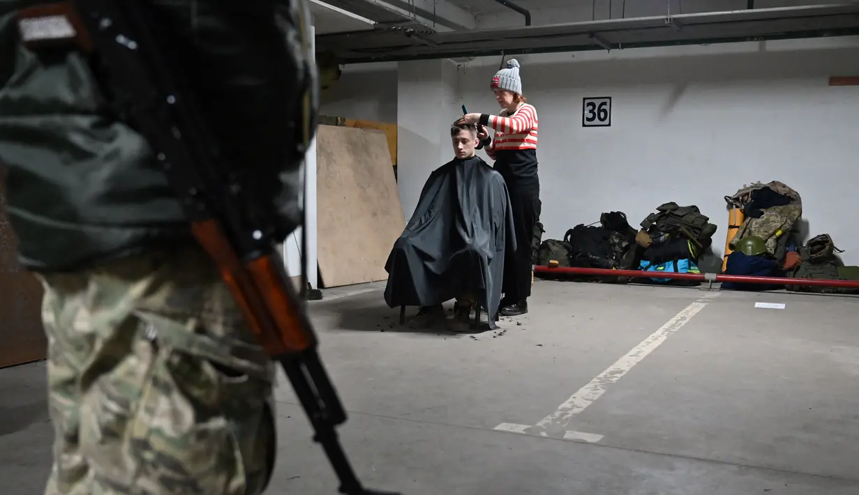 Seorang penata rambut memotong rambut seorang prajurit Pasukan Pertahanan Teritorial Ukraina, cadangan militer Angkatan Bersenjata Ukraina, di garasi bawah tanah yang telah diubah menjadi pangkalan pelatihan dan logistik di Kiev, pada Jumat (11/3/2022). (Sergei SUPINSKY / AFP)