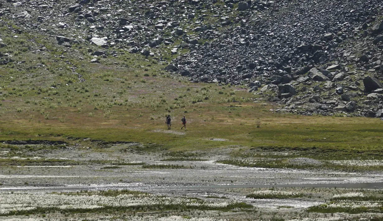 Pendaki berjalan di atas hamparan kering danau buatan Gabiet dekat Gressoney-La-Trinite di Lembah Aosta, Italia utara, Selasa (19/7/2022). Kekeringan parah masih melanda bagian utara negara itu. (AP Photo/Luca Bruno)