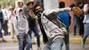 Mahasiswa Venezuela Central University melempar batu ke arah polisi selama protes menuntut peningkatan anggaran beasiswa dan membuka kembali kafetaria universitas di Caracas, Venezuela (21/11). (AP Photo/Ariana Cubillos)