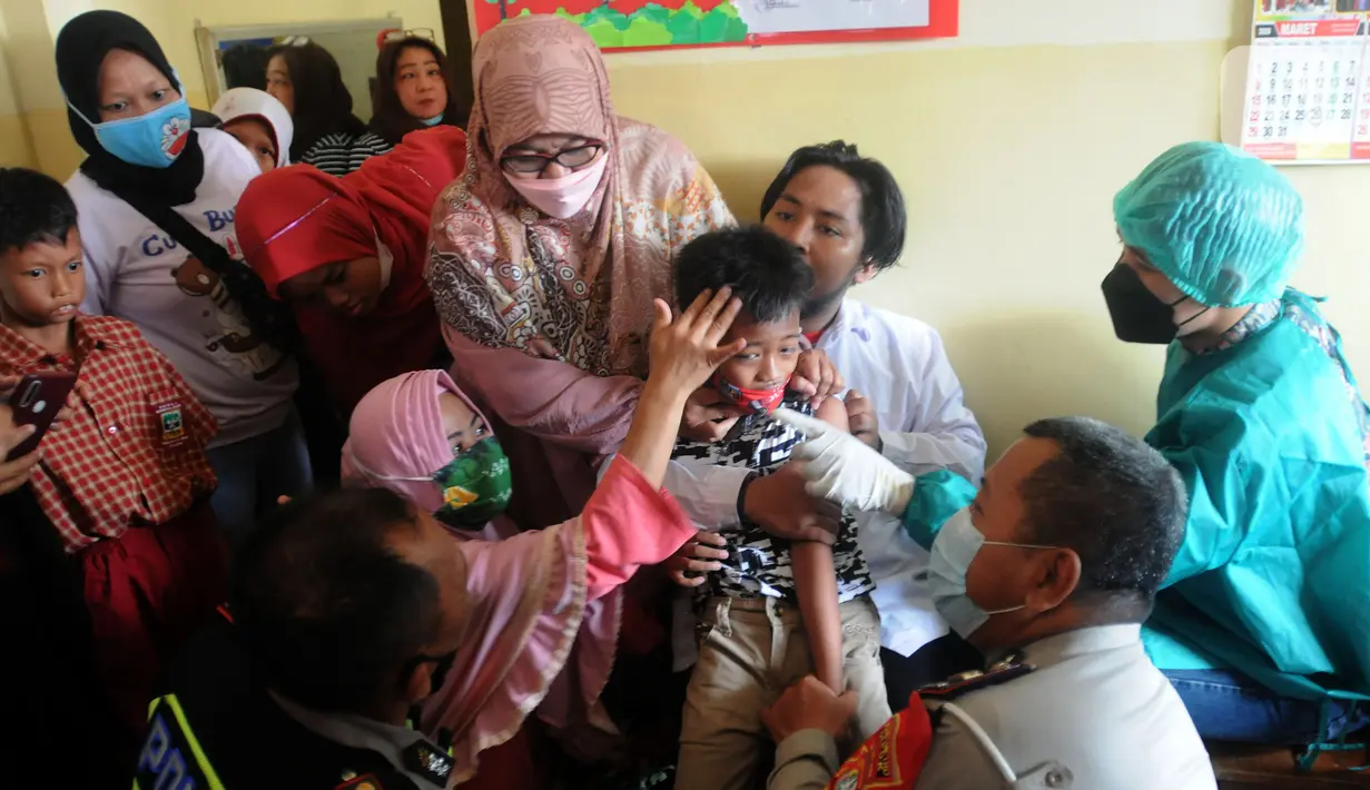 Anggota Polri dari Polsek Cinere memegangi murid penyandang tunagrahita yang akan disuntik vaksin COVID-19 di SLB BC Manunggal Bhakti, Depok, Selasa (11/1/2022). Delapan murid SLB disuntik vaksin COVID-19 Sinovac yang merupakan rangkaian program Vaksinasi Merdeka. (merdeka.com/Arie Basuki)