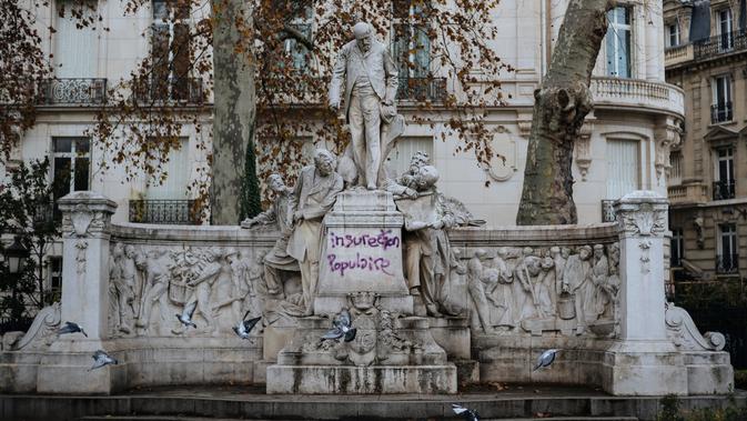 Grafiti bertuliskan 'insureksi populer' tertulis pada patung dekat Arc de Triomphe, Paris, Prancis, Minggu (2/12). Rakyat menuding kenaikan pajak bahan bakar berdampak pada risiko meningkatnya biaya hidup. (AP Photo/Kamil Zihnioglu)