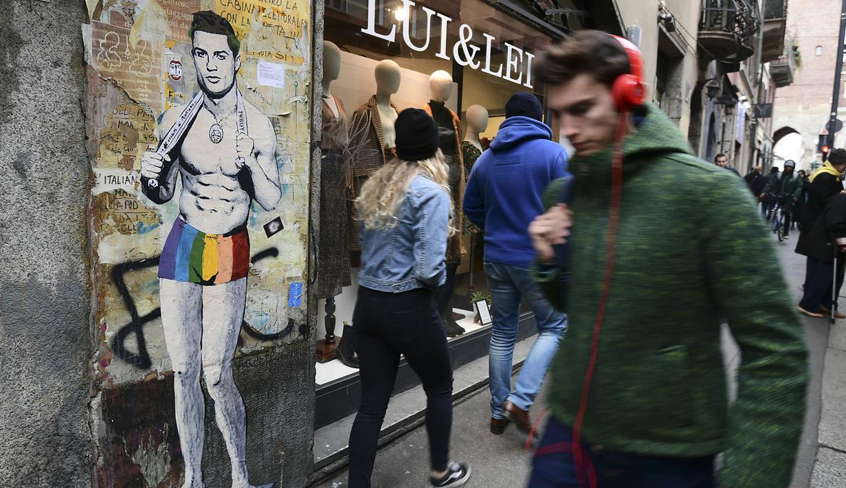 Sejumlah warga melintasi mural dengan gambar bintang Juventus, Cristiano Ronaldo, yang terdapat di Milan, Senin (19/3). Mural berjudul Cristiano's Secret ini karya seniman Italia, TvBoy. (AFP/Miguel Medina)