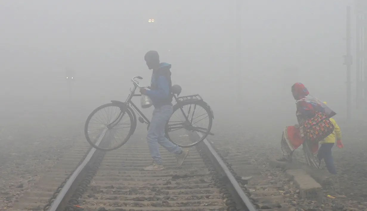 Keluarga menyebrangi jalur kereta api saat kabut tebal di Jalandhar (25/12). India Utara dilanda kabut pagi yang pekat dalam beberapa hari terakhir saat suhu dingin dan kondisi angin rendah turun di wilayah tersebut. (AFP Photo/Shammi Mehra)