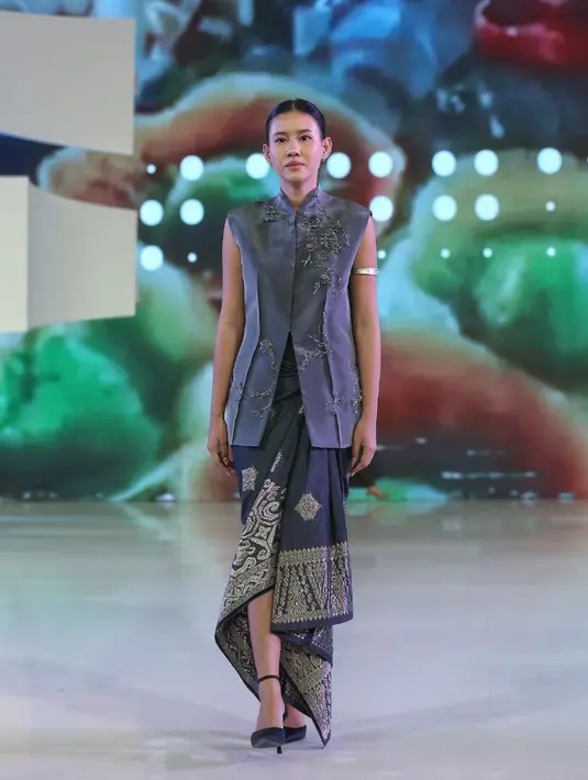 Shenina Cinnamon kenakan atasan vest warna abu-abu kerah tinggi dengan aksen beads warna senada. Dipadukan bawahan kain songket hitam bordir emas serta high heels hitamnya. [Adrian/Fimela]