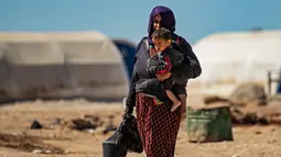 Seorang wanita Suriah yang terlantar berjalan dengan anaknya dan kantong-kantong belanjaan selama bulan suci Ramadan di kamp Washukanni untuk para pengungsi internal di provinsi Hasakeh di timur laut Suriah, (10/5/2020). (AFP/Delil Souleiman)