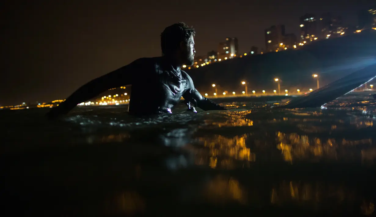 Ernesto Benavides menunggu datangnya ombak dari Samudra Pasifik saat akan berselancar di pantai La Pampilla, ibu kota Peru, Lima, 8 Maret 2017. Sekelompok peselancar hardcore memilih bermain selancar pada malam hari. (AP Photo/Rodrigo Abd)