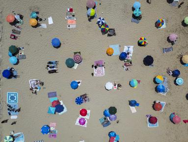 Foto udara menunjukkan orang-orang berjemur di pantai Costa da Caparica di Almada, dekat Lisbon, selama gelombang panas pertama tahun ini, pada tanggal 29 Juni 2025. (CARLOS COSTA/AFP)