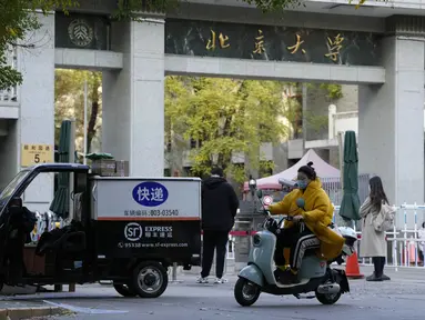 Seorang perempuan yang mengenakan masker melewati pintu masuk Universitas Peking di Beijing, Rabu (16/11/2022). Pihak berwenang China mengunci Universitas Peking setelah temuan satu kasus virus Corona Covid-19 di area kampus. (AP Photo/Ng Han Guan)