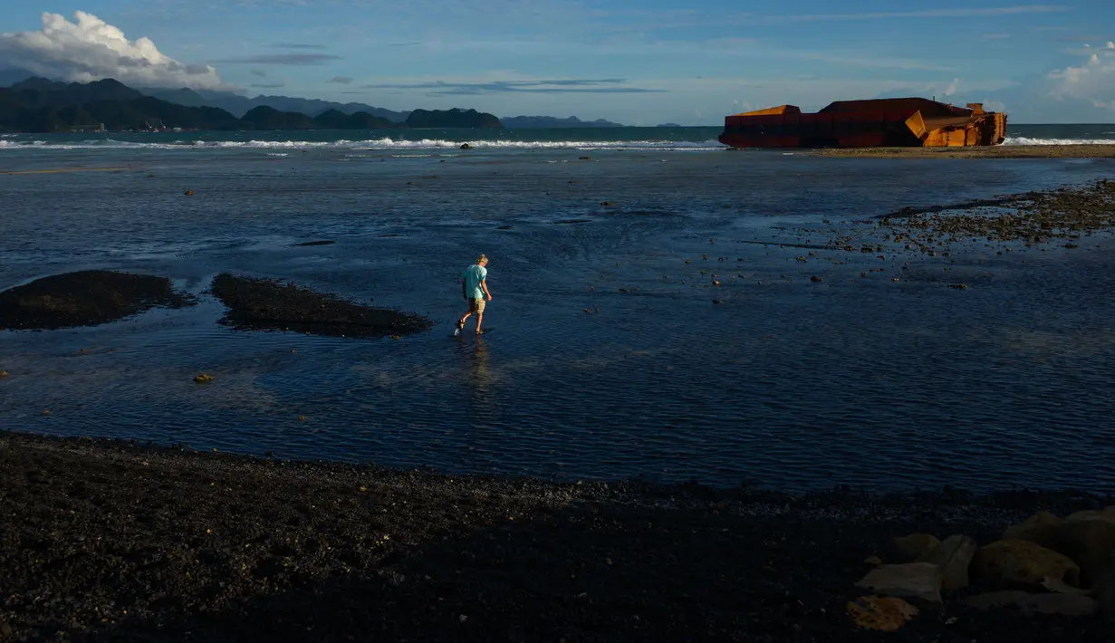 Seorang pria berjalan di pantai Lhoknga yang tercemar tumpahan batu bara dari sebuah tongkang di Aceh, Rabu (1/8). Sekitar 7.000 ton batu bara tumpah dari kapal tongkang yang kandas dihantam gelombang sehingga mencemari pantai. (AFP/CHAIDEER MAHYUDDIN)