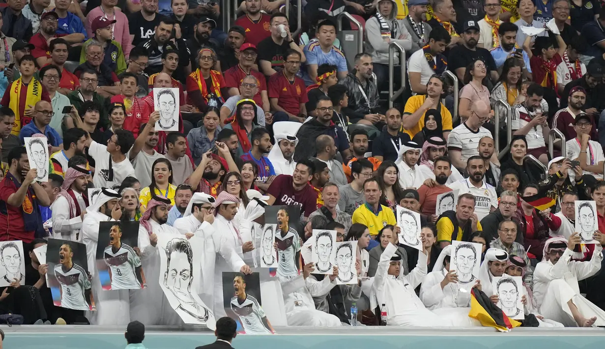Penonton memegang foto Mesut Ozil di tribun selama pertandingan Spanyol vs Jerman pada laga Grup E Piala Dunia 2022  di Stadion Al Bayt, Kota Al Khor, Senin (28/11/2022) dini hari WIB. Para penonton menuduh timnas Jerman dan DFB tidak bersikap 'adil' terhadap Mesut Ozil. (AP Photo/Matthias Schrader)