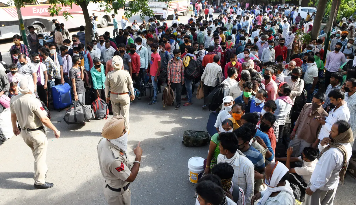 Personel polisi berjaga saat pekerja migran dan keluarga mereja antre menunggu pemeriksaan medis sebelum menaiki kereta untuk kembali ke kota asal mereka ke Jaunpur, negara bagian Uttar Pradesh, setelah pemerintah melonggarkan lockdown di Amritsar, India, Selasa (19/5/2020). (NARINDER NANU/AFP)