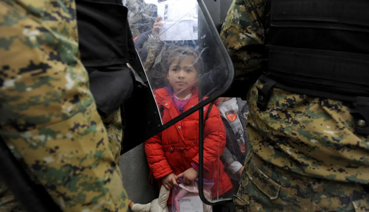 Seorang gadis migran memegang mainan di perbatasan Yunani-Macedonia (20/11/2015). Polisi melakukan penjagaan  dan mencegah para imigran untuk masuk ke negaranya. (REUTERS / Alexandros Avramidis)