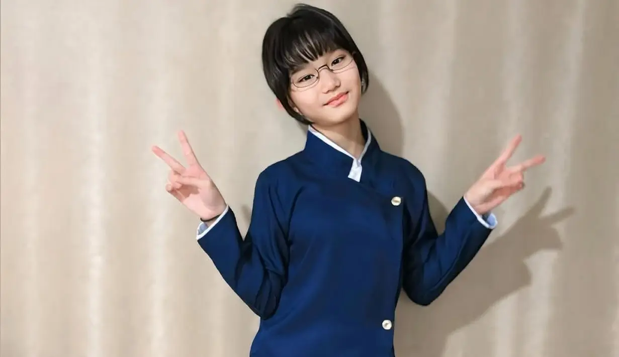 Atasan yang dikenakan Bilqis memiliki desain asimetris dengan kancing emas yang memberikan sentuhan elegan. Kerah putih tinggi semakin memperkuat kesan khas Jepang, dipadukan dengan celana panjang biru tua yang serasi. Rambut pendek berponi serta kacamata yang dikenakannya membuatnya semakin mirip karakter dalam anime atau drama Jepang. (Liputan6.com/IG/@ayutingting92)